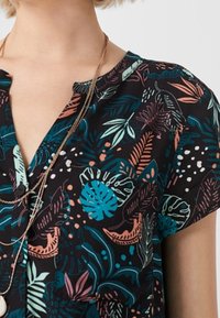Blusa a maniche corte con sfondo nero e motivi di piante tropicali colorate in turchese, rosa e arancione. Scollo a V e tessuto morbido.