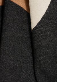 Tela de mezclilla negra con un leve brillo, que presenta una textura granulada y patrones de tejido visibles; acentos de tela en beige claro y marrón adicionales.
