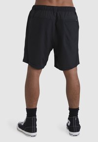 Shorts de sport noirs avec une taille élastique, comportant des poches latérales et une poche zippée au dos. Portés avec des baskets montantes noires.