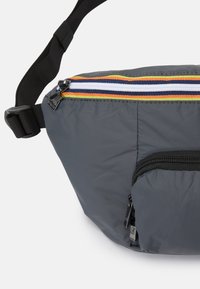 Grå nylon magasin med en horisontal stribet lynlås i rød, blå, orange og grøn. Har en frontlynlåslomme og justerbar rem.