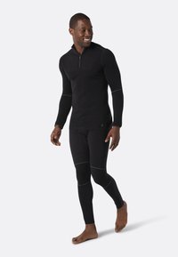 Zwarte thermoshirt met een halve rits en lange mouwen, gecombineerd met bijpassende aansluitende leggings. Voorzien van witte stikselaccenten.