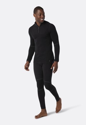 Maglia termica nera con colletto a mezza zip e maniche lunghe, abbinata a leggings aderenti abbinati. Presenta dettagli di cucitura bianchi.
