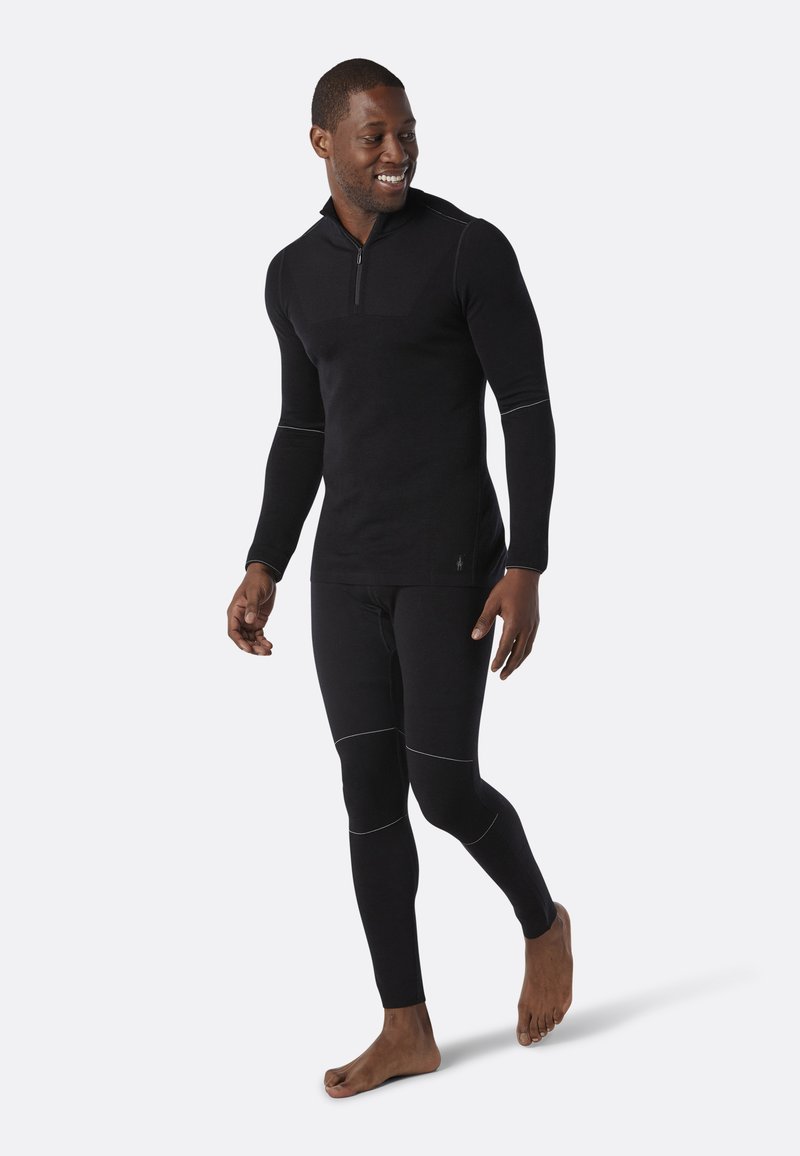 Zwarte thermoshirt met een halve rits en lange mouwen, gecombineerd met bijpassende aansluitende leggings. Voorzien van witte stikselaccenten.
