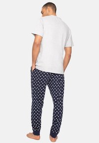 Graues Baumwoll-T-Shirt kombiniert mit marineblauen Schlafanzughosen, die mit weißen Sternenmustern verziert sind. Die Hosen haben gerippte Bündchen und Taschen.