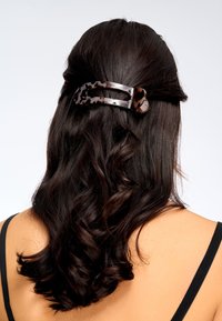 Cheveux ondulés brun foncé attachés à moitié, maintenus avec une grande pince à cheveux motif écaille de tortue, visible de dos.