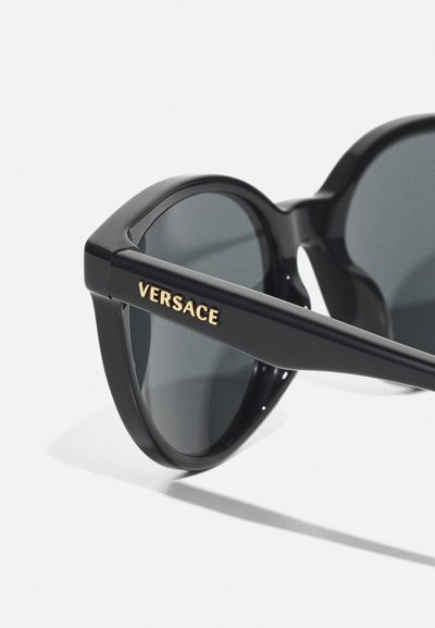 Juodi plastikiniai saulės akiniai su apvaliais lęšiais, su auksiniu "VERSACE" logotipu ant šventyklos. Sklandus paviršius ir ryškus, modernus dizainas.