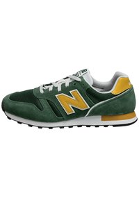 Chaussure de sport en daim vert et mesh avec des accents jaunes et des lacets blancs. Elle présente une tige texturée et une semelle en caoutchouc pour une bonne adhérence.