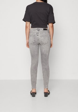 Jeans ajustados grises de cintura alta y efecto desgastado, combinados con una camiseta negra corta. El calzado incluye tacones gruesos negros.