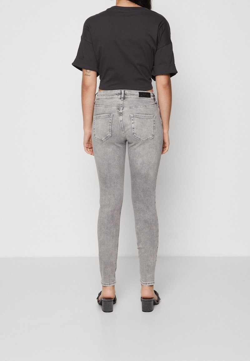 Jeans ajustados grises de cintura alta y efecto desgastado, combinados con una camiseta negra corta. El calzado incluye tacones gruesos negros.