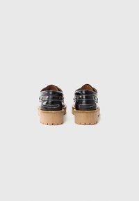Schwarze Lederschuhe mit strukturiertem Obermaterial, verstellbaren Riemen und starker, beiger Sohle mit gezacktem Muster. Rückansicht gezeigt.