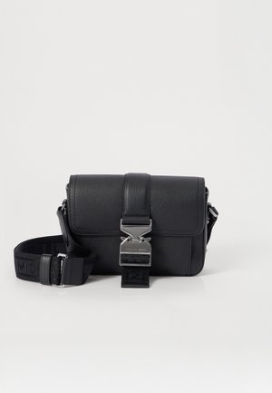 Bolso cruzado de piel negra con acabado texturizado, herrajes plateados, cierre de hebilla y correa desmontable con un patrón de logo.