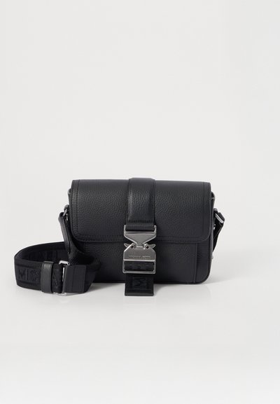 Sac à bandoulière en cuir noir avec une finition texturée, quincaillerie en argent, fermeture à boucle et une sangle détachable arborant un motif de logo.
