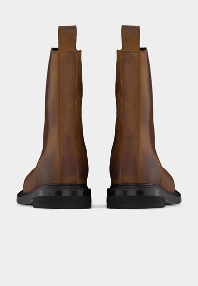 Paire de bottines en cuir marron avec semelles noires vues de dos, montrant les languettes de tirage et les détails de couture.