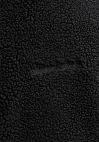 Schwarzer Fleece-Stoff mit strukturierter Oberfläche, versehen mit einem dezenten gestickten Logo zur Markenidentifikation. Weich, dick und einheitlich in Farbe und Muster.