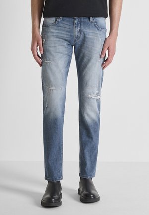 Vaqueros de mezclilla azul claro con detalles desgastados, diseño de pierna recta y estilo de cinco bolsillos. Llevados con botas negras hasta el tobillo.