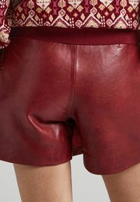 Rode leren shorts met een gladde textuur en een aansluitende tailleband. Het ontwerp heeft minimale stiksels en een strakke, eigentijdse vorm.