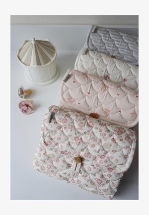 Four quilted fabric pouches with floral, bow, and striped patterns aligned on a white surface beside three pacifiers and a white carousel.