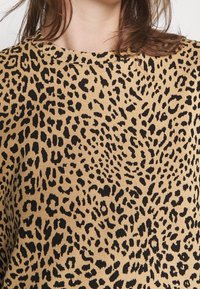 Top con estampado de leopardo que presenta un fondo beige con manchas negras, cuello redondo y textura de tela suave.