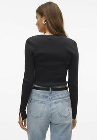Top a maniche lunghe nero a coste con scollatura rotonda, con dettagli bianchi alle aperture delle maniche, abbinato a jeans a vita alta di un blu chiaro.