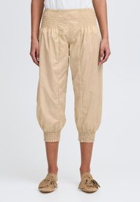 Pants en coton beige avec une taille smockée et des poignets resserrés. Le matériau semble léger avec une texture lisse.