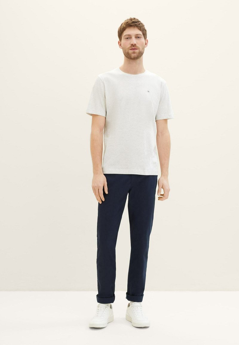 Lys grå bomulds t-shirt med rund hals, parret med marineblå bukser og hvide sneakers, præsenteret på en neutral baggrund.