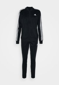 Czarny dres Adidas z białymi paskami na rękawach i nogawkach, bluza na zamek oraz logo Adidas na piersi i udzie.