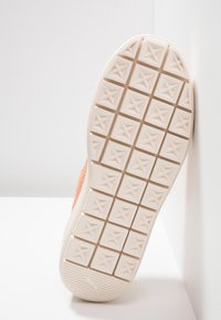 Sole sportovní obuvi, světle béžová s texturovaným vzorem pro grip, obsahující čtvercové tvary a logo značky. Horní část je vyrobena z oranžové semišové látky.