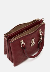 Burgundy nahkakäsilaukku, jossa on kaksinkertaiset vetoketjusektorit, kultaiset yksityiskohdat, kohokuvioitu malli ja yläkahvat kantamista varten.