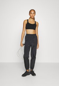Top cropped atlético preto com alças ajustáveis, combinado com calças jogger leves pretas com punhos elásticos. Segurando uma corda de pular.