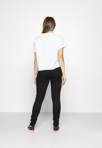 Camiseta blanca de manga corta con un corte relajado, combinada con pantalones negros ajustados y zapatillas burdeos, vista desde la parte de atrás.
