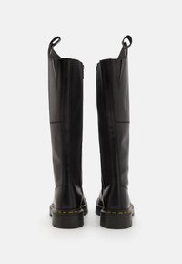 Black leather knee-high boots featuring a smooth finish, sturdy rubber soles, yellow stitching details, and pull tabs for easy wear.