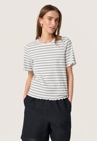 Camiseta blanca de manga corta con rayas horizontales negras, dobladillo festoneado y escote redondo, combinada con pantalones cortos de lino oscuros.