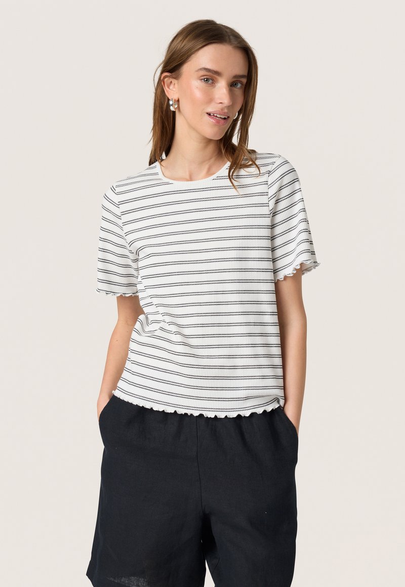 Camiseta blanca de manga corta con rayas horizontales negras, dobladillo festoneado y escote redondo, combinada con pantalones cortos de lino oscuros.