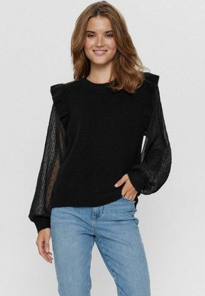 Schwarzer Pullover mit strukturiertem Oberteil, gerafften Schulterakzenten und transparenten langen Ärmeln mit Punkte-Muster. Kombiniert mit blauen Jeans.