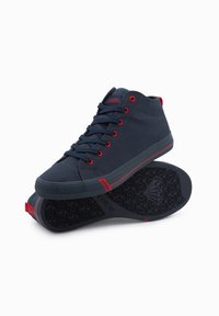 Hochschnitt-Sneaker aus marineblauem Canvas mit roten Akzenten. Verfügt über runde Schnürsenkel, eine Gummisohle und eine strukturierte Außensohle für besseren Grip. Branding ist an der Seite sichtbar.