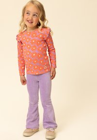 Oranje blouse met bloemenpatroon, geribbelde textuur en ruches aan de mouwen. Gecombineerd met paarse flared ribfluwelen broek en beige sneakers.