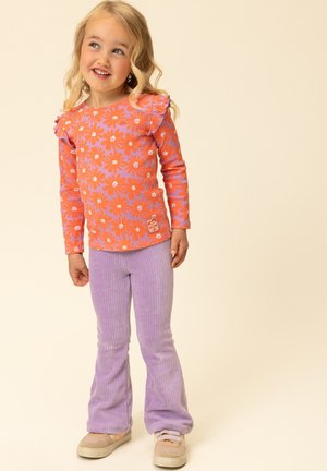 Oranje blouse met bloemenpatroon, geribbelde textuur en ruches aan de mouwen. Gecombineerd met paarse flared ribfluwelen broek en beige sneakers.