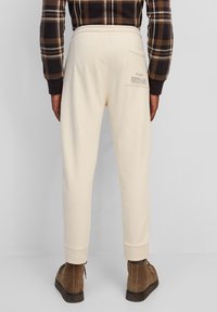 Helle beige Jogginghose aus weichem Material mit gerippten Bündchen und einer Gesäßtasche mit Druckdetails. Kombiniert mit braunen Stiefeln.