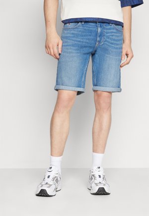 Pantalones cortos de denim azul claro con dobladillos enrollados, que presentan un diseño clásico de cinco bolsillos y un ligero desvanecimiento. Se llevan con calcetas deportivas blancas y zapatos.