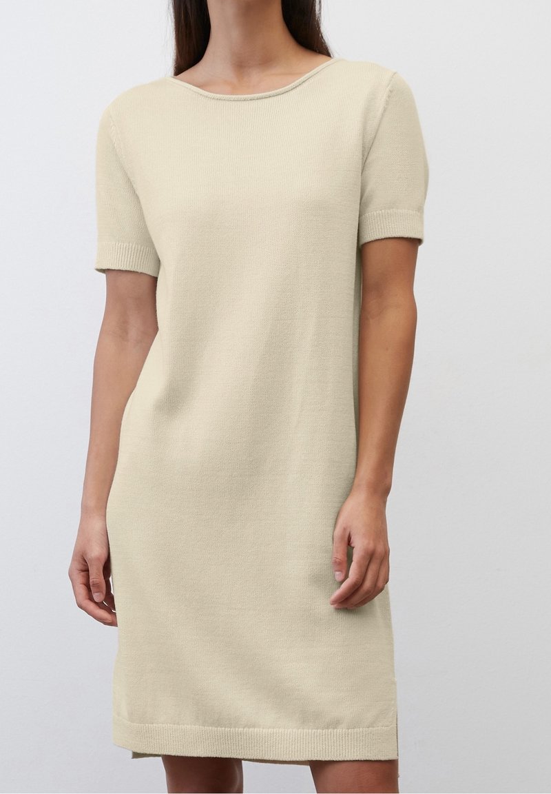 Abito lavorato a maglia beige con maniche corte, scollatura a giro e orli a coste. Presenta una vestibilità rilassata e una texture liscia.