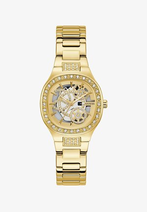 Gull klokke med en skeleton-design, krystallakkenter rundt bezel, og en gull-tone armbånd. Har en hvit skive med svart detaljering.