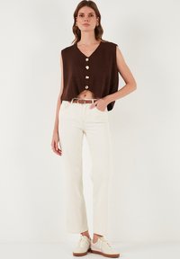 Brązowy krótki top bez rękawów z dekoltem w serek i czterema złotymi guzikami, połączony z białymi spodniami z wysokim stanem oraz beżowymi trampkami.