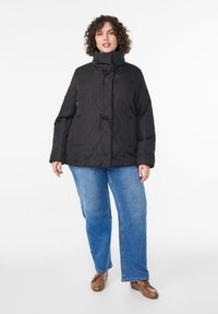 Čierna prešívaná bunda s vysokým golierom, so zapínaním na cvoky a dvoma bočnými vreckami, nosená cez modré rifle s priamymi nohavicami.