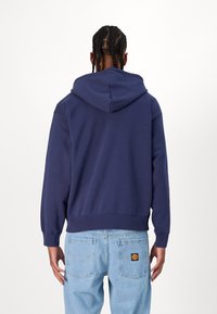 Navy blue hoodie with a drawstring hood, ribbed cuffs and hem, soft texture, and a relaxed fit, paired with light blue jeans.