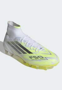 Λευκό ποδοσφαιρικό παπούτσι με νέον κίτρινο, κάλτσα στον αστράγαλο, διαφανείς καρφίτσες στη σόλα, μαύρες ρίγες και κείμενο "F50 Sparkfusion" στο πλάι.