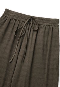 Tmavě zelená, texturovaná látka s žebrovaným vzorem. Má elastický pas se stahovací šňůrkou pro nastavitelnou velikost.