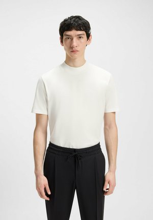 Weißes Kurzarmhemd mit hohem Kragen, kombiniert mit schwarzen Hosen mit elastischem Bund und Kordelzug. Glatte Textur.