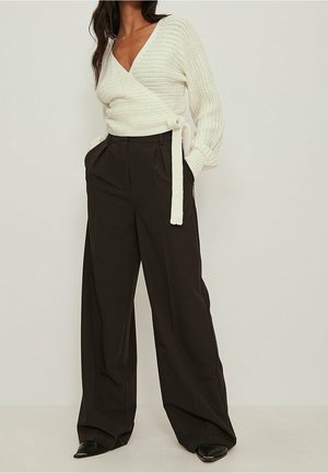 Witte gebreide wraptrui met een V-halslijn, gecombineerd met hoge zwarte broeken met een brede pijp.