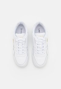 Paire de baskets blanches Lacoste avec lacets, nom de la marque visible sur la languette et semelles ortholite, vues de dessus sur fond blanc.