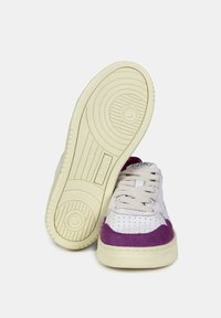 Sneakers bianchi con accenti in suede viola, suola in gomma testurizzata, lacci piatti e area delle dita perforata, con un marchio discreto sulla linguetta.